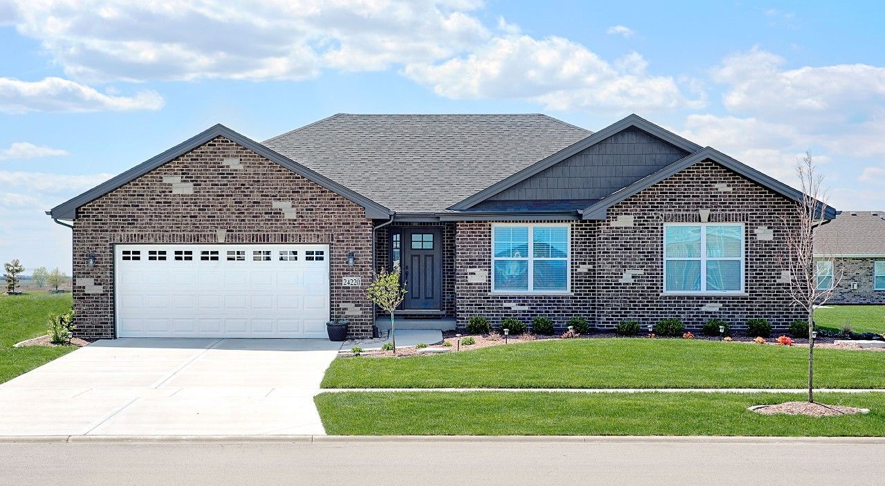 A large brick house with a white garage door is sitting on top of a lush green field.