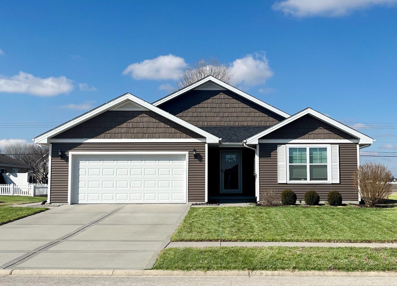 A brown and white house with a large garage and a concrete driveway.