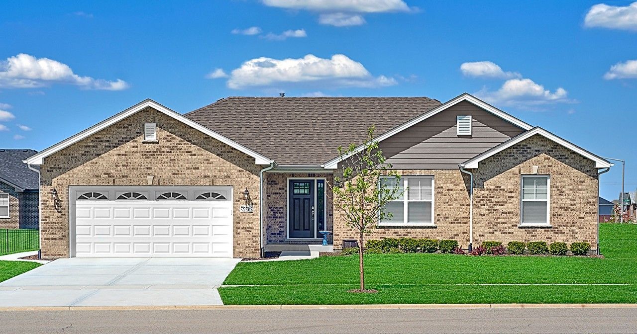 A large brick house with a white garage door is sitting on top of a lush green lawn.
