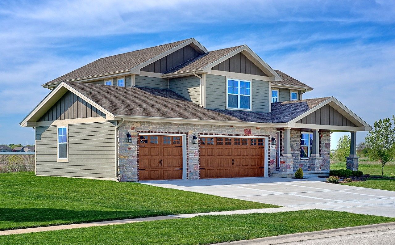 A large house with two garage doors is sitting on top of a lush green field.