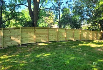 A wooden fence is surrounded by trees in a backyard.
