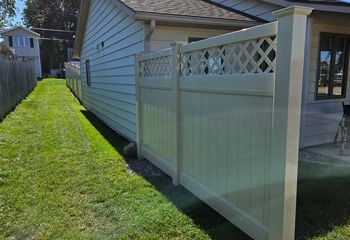 A white fence surrounds a lush green yard next to a house.