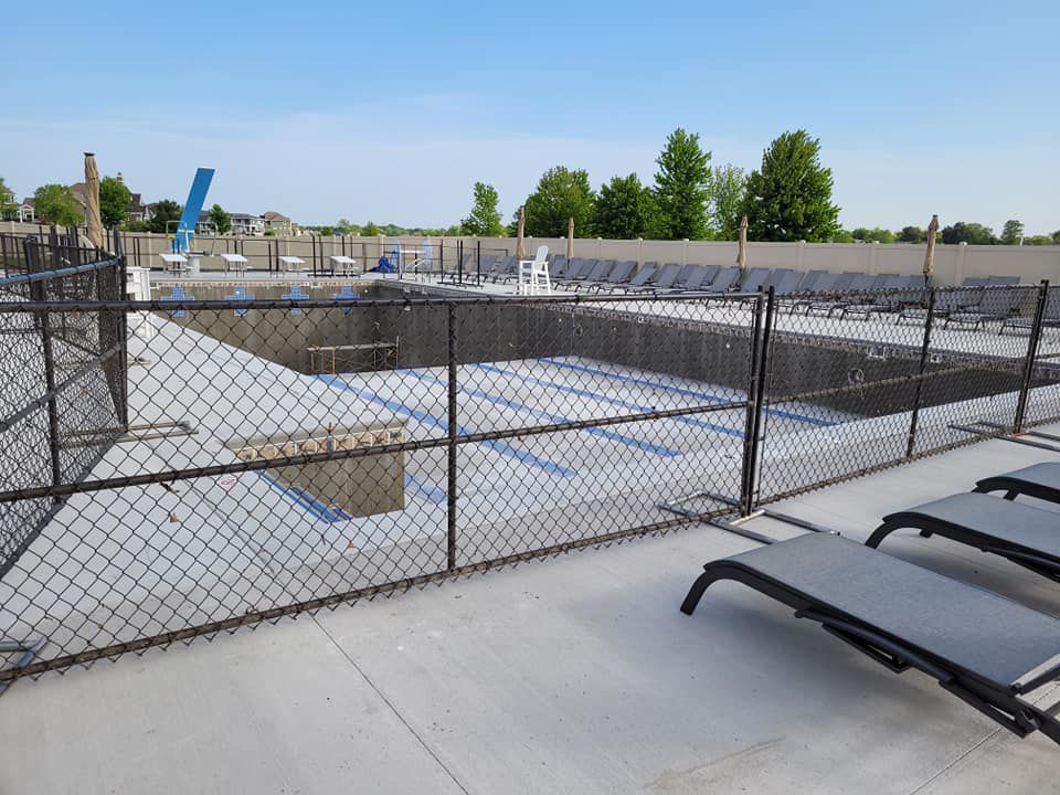 A chain link fence surrounds a large swimming pool.