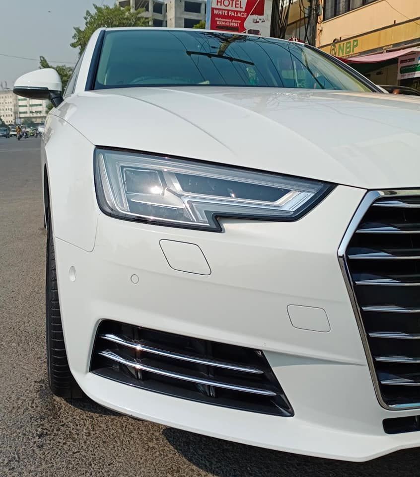 White Audi sedan parked on a city street. Front view showing headlights and grille.