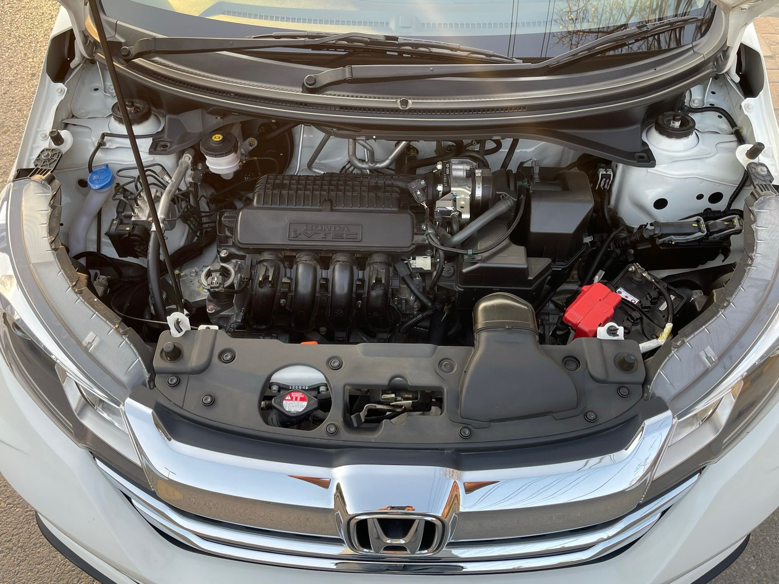 Open car hood revealing a clean engine. White car, various black engine components, silver trim.