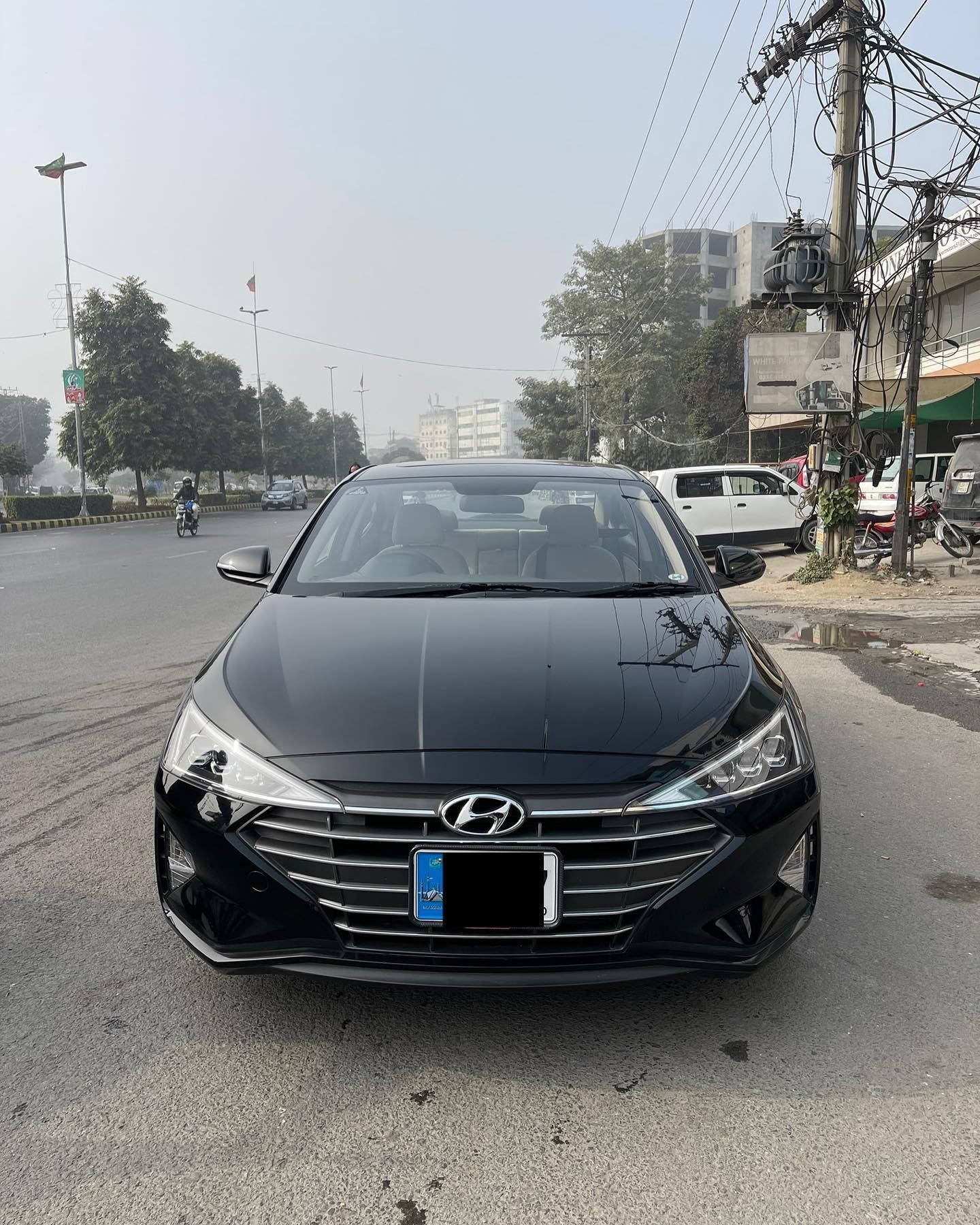 Black Hyundai Elantra parked on a city street. Grey sky, buildings, and other cars in the background.