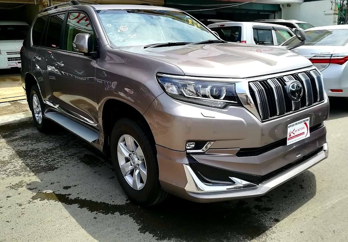 Brown Toyota Land Cruiser Prado parked on a wet surface, under a building.