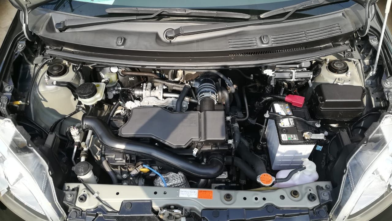 Car engine bay, black, with various components visible. Battery and reservoir tanks are present.