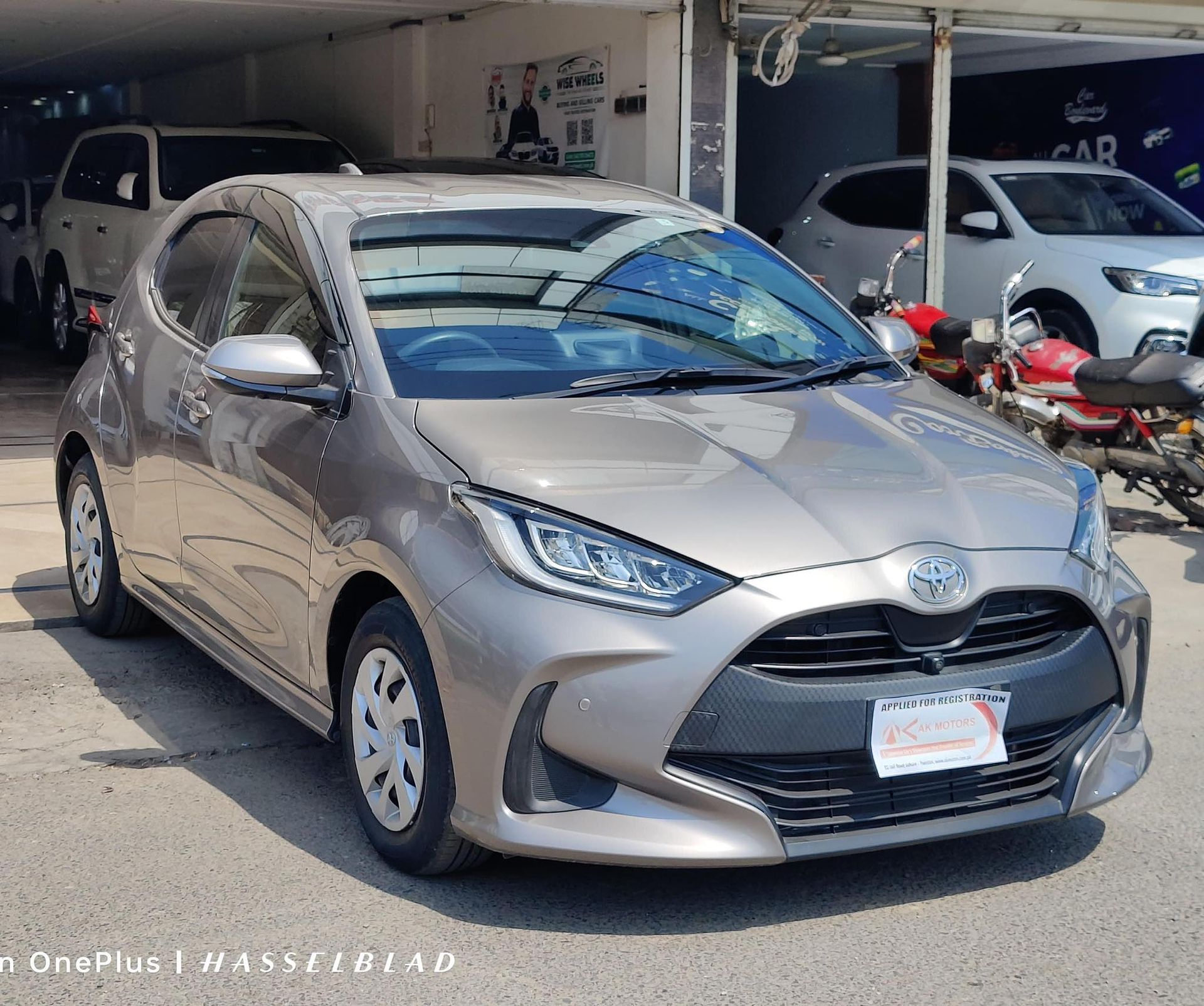Tan Toyota Yaris hatchback parked outdoors in front of a car dealership.