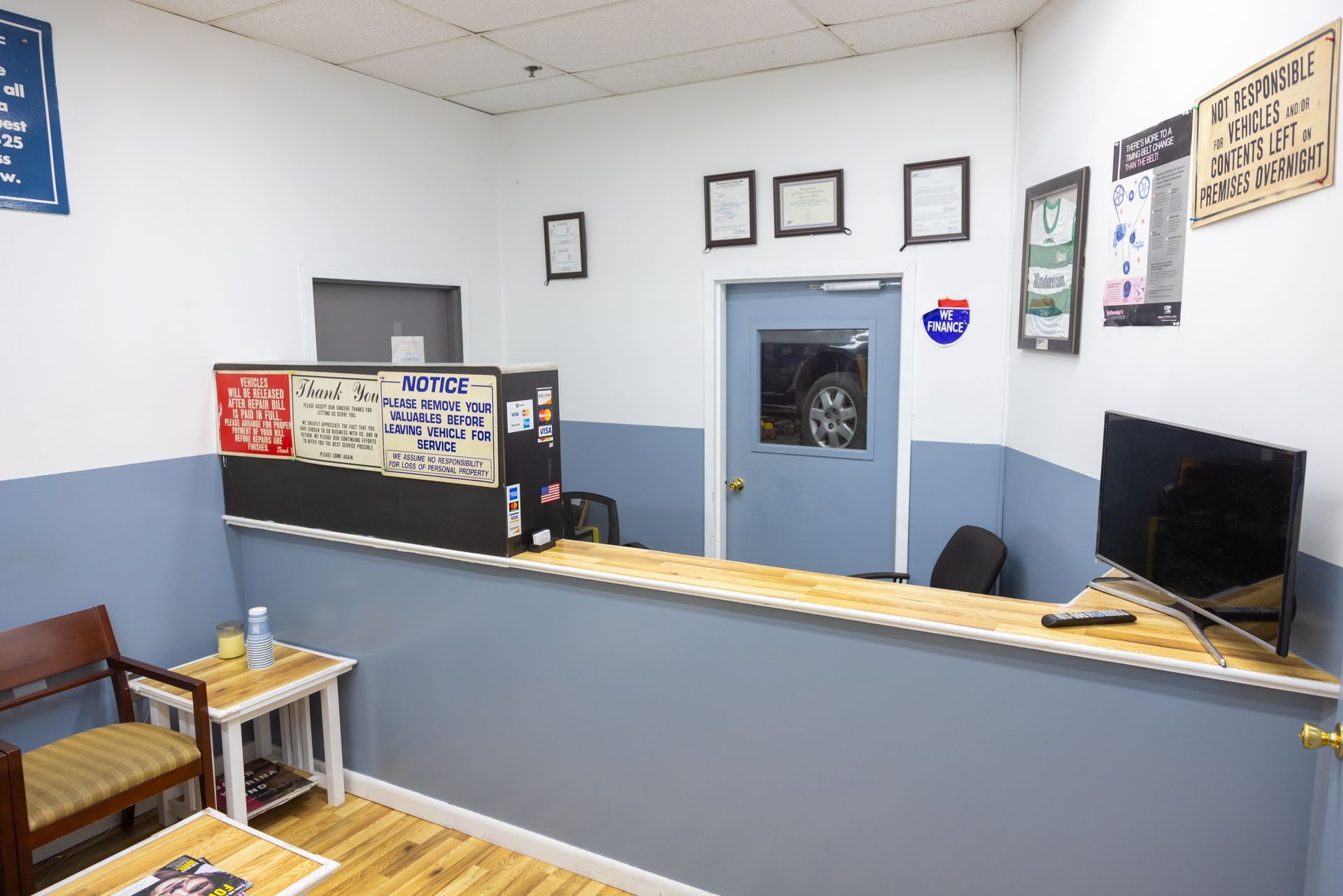 An auto repair shop's waiting area. Gray and white walls, a counter, waiting chairs, and a TV.
