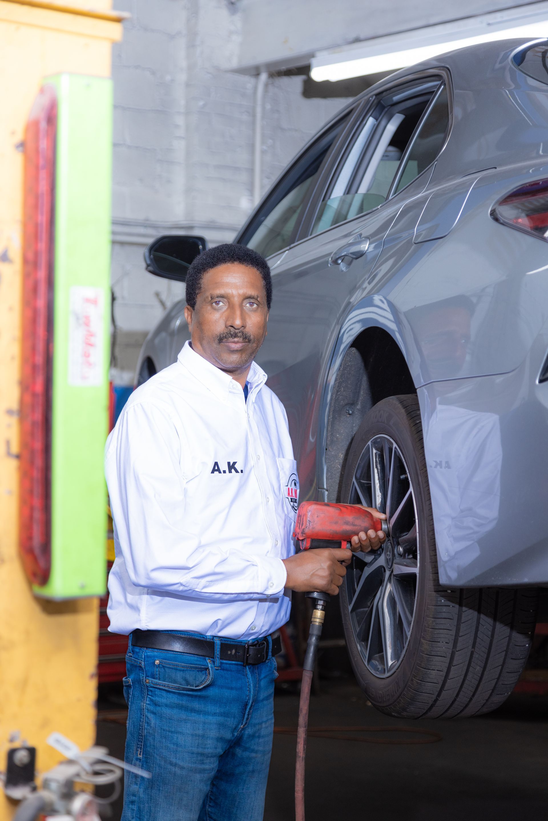 Mechanic using a power tool on a car's tire in a garage.