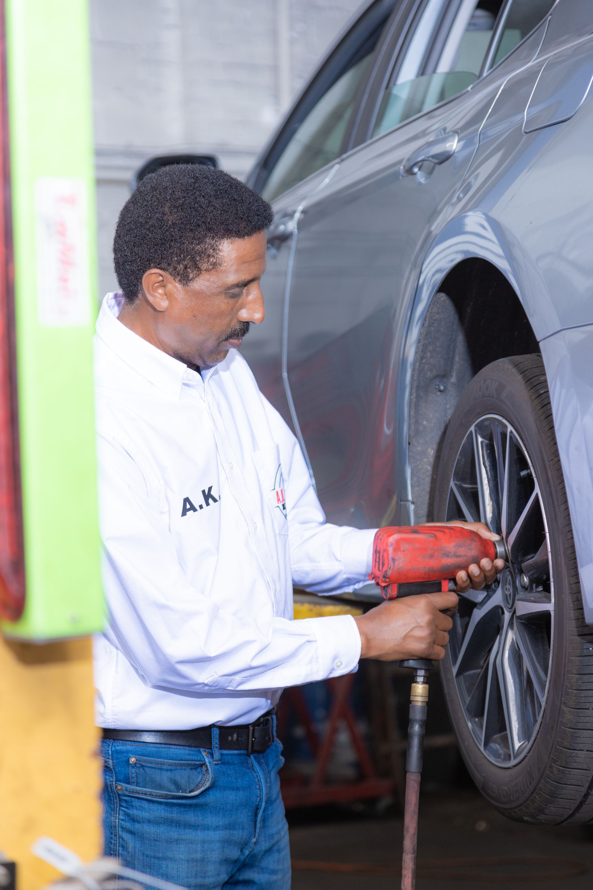 Mechanic using a pneumatic wrench on a car tire, in a repair shop.
