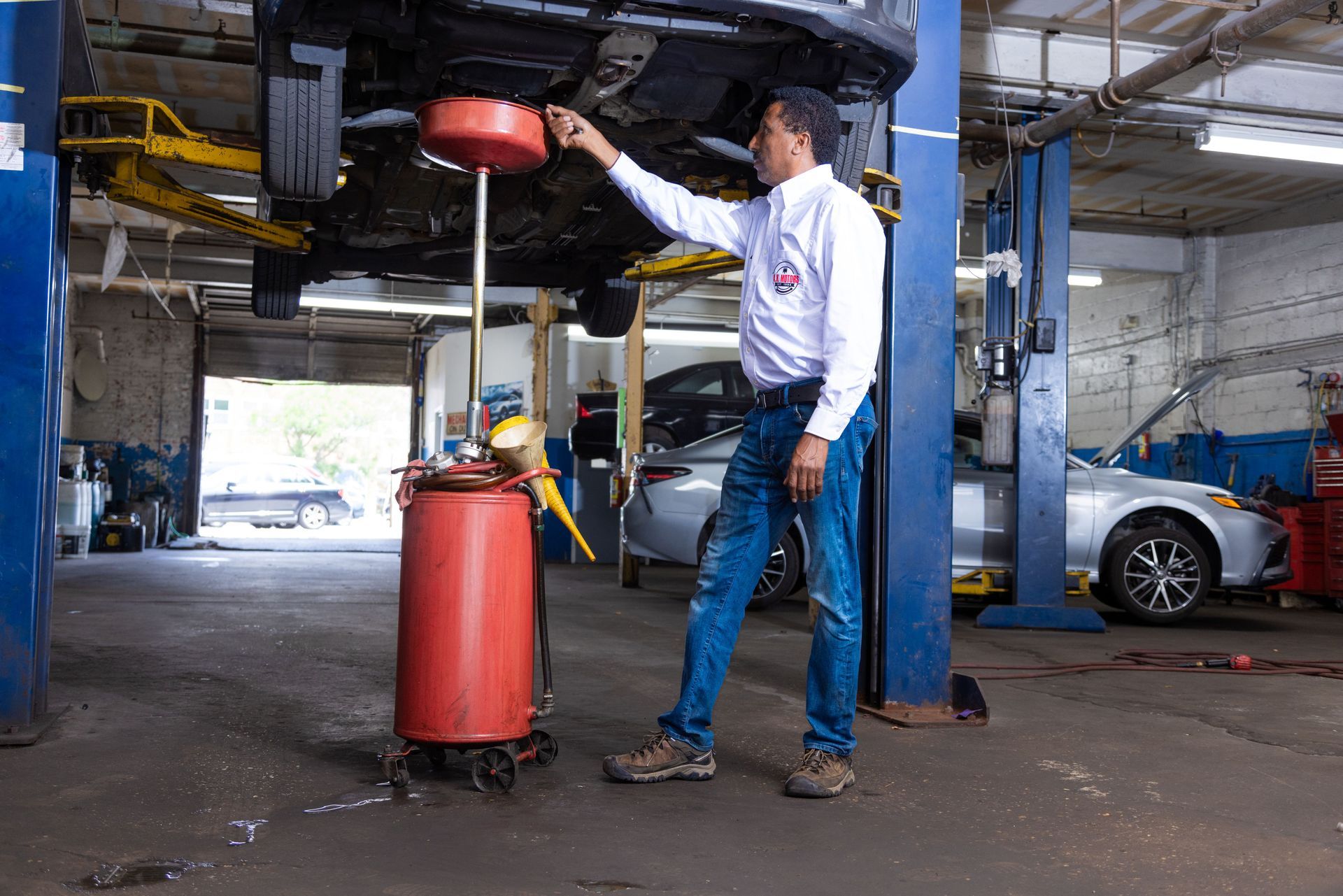 Mechanic draining oil from a car at a repair shop, using a container.