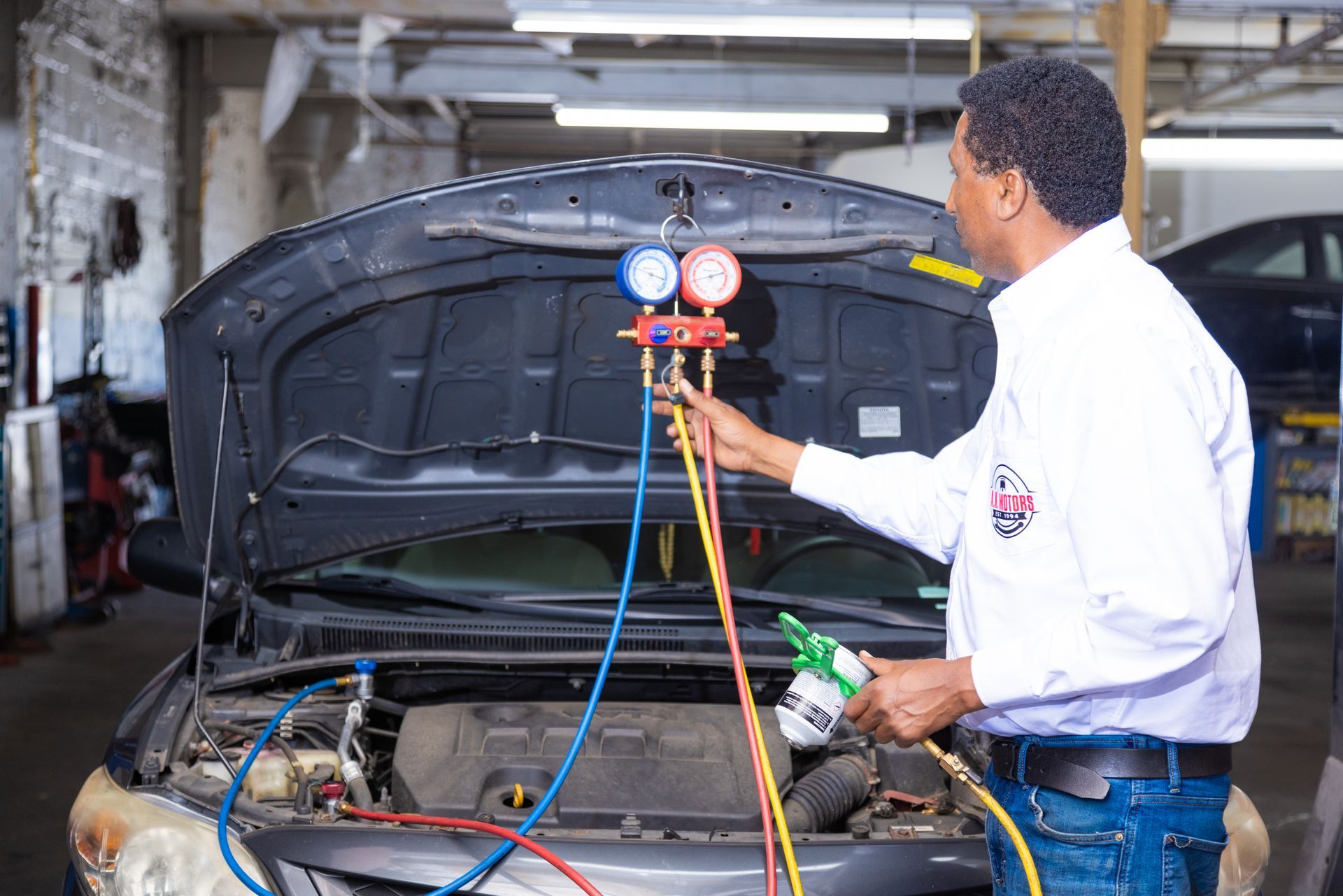 Mechanic checking car AC with gauges in a garage.