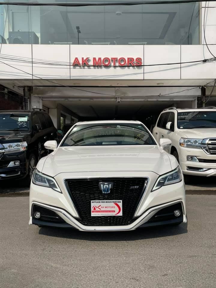 White Toyota Crown sedan in front of AK Motors dealership.