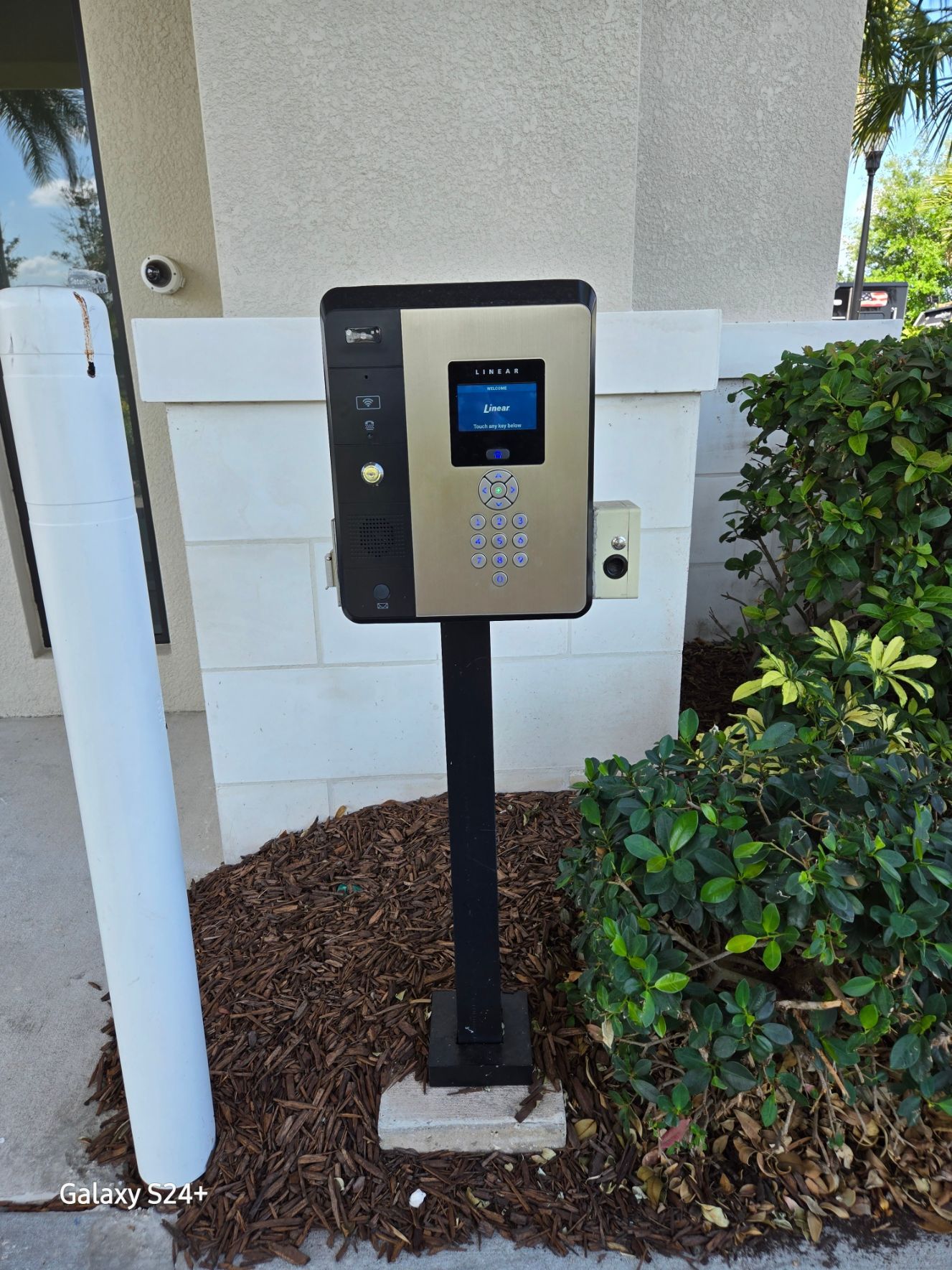 A keypad is sitting on a pole in front of a building.