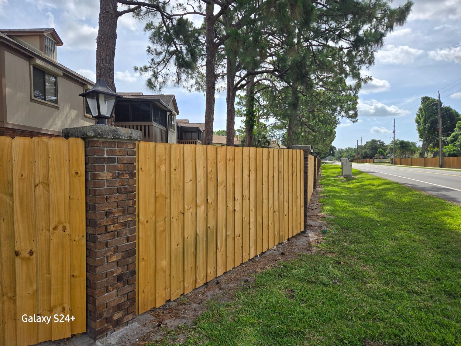 A wooden fence surrounds a brick wall on the side of a road.