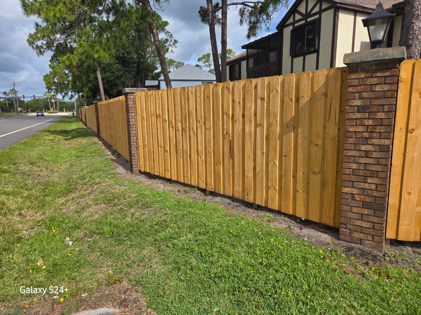 A wooden fence surrounds a brick wall in front of a house.