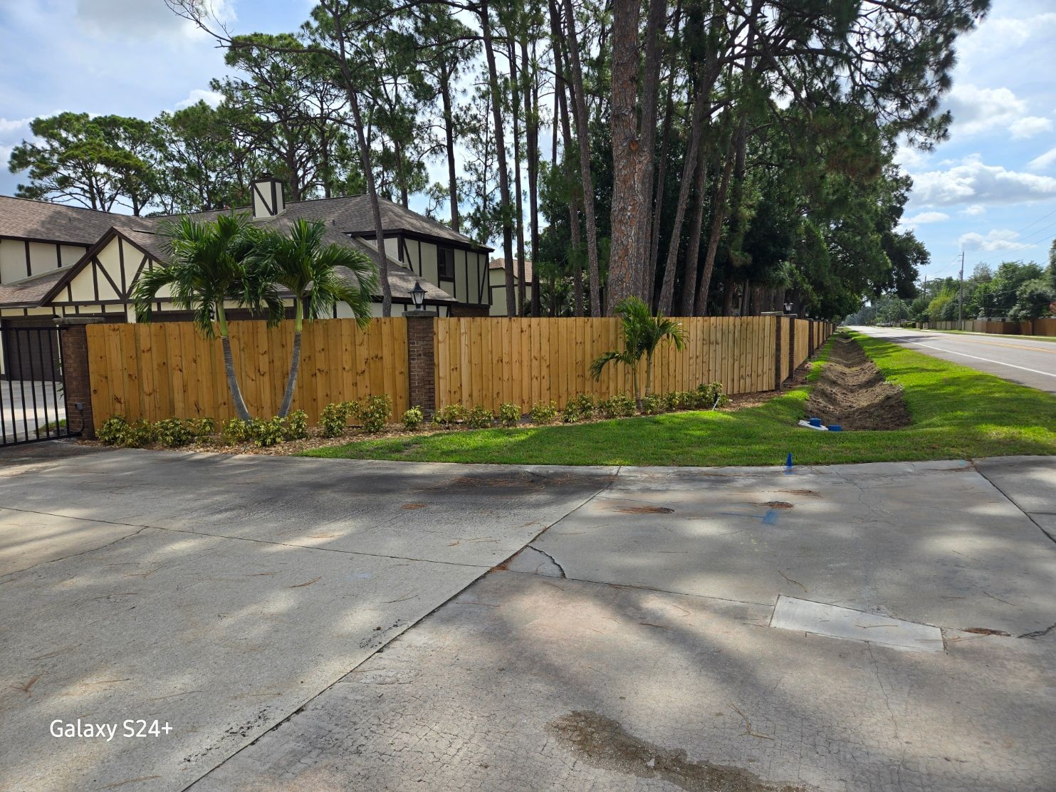 A wooden fence is along the side of a road next to a house.