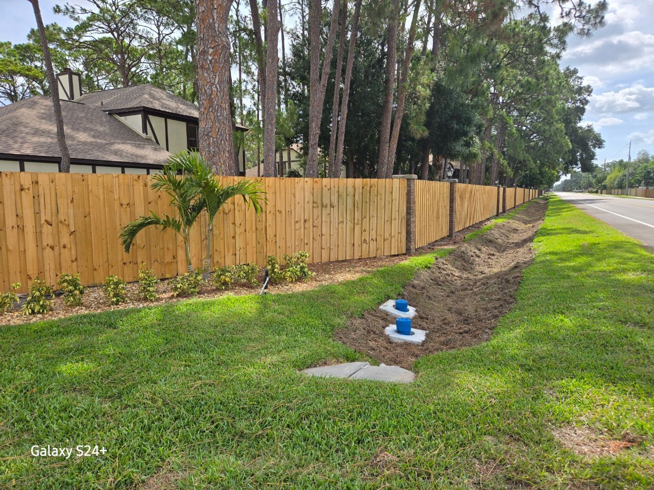 A wooden fence along the side of a road next to a house.