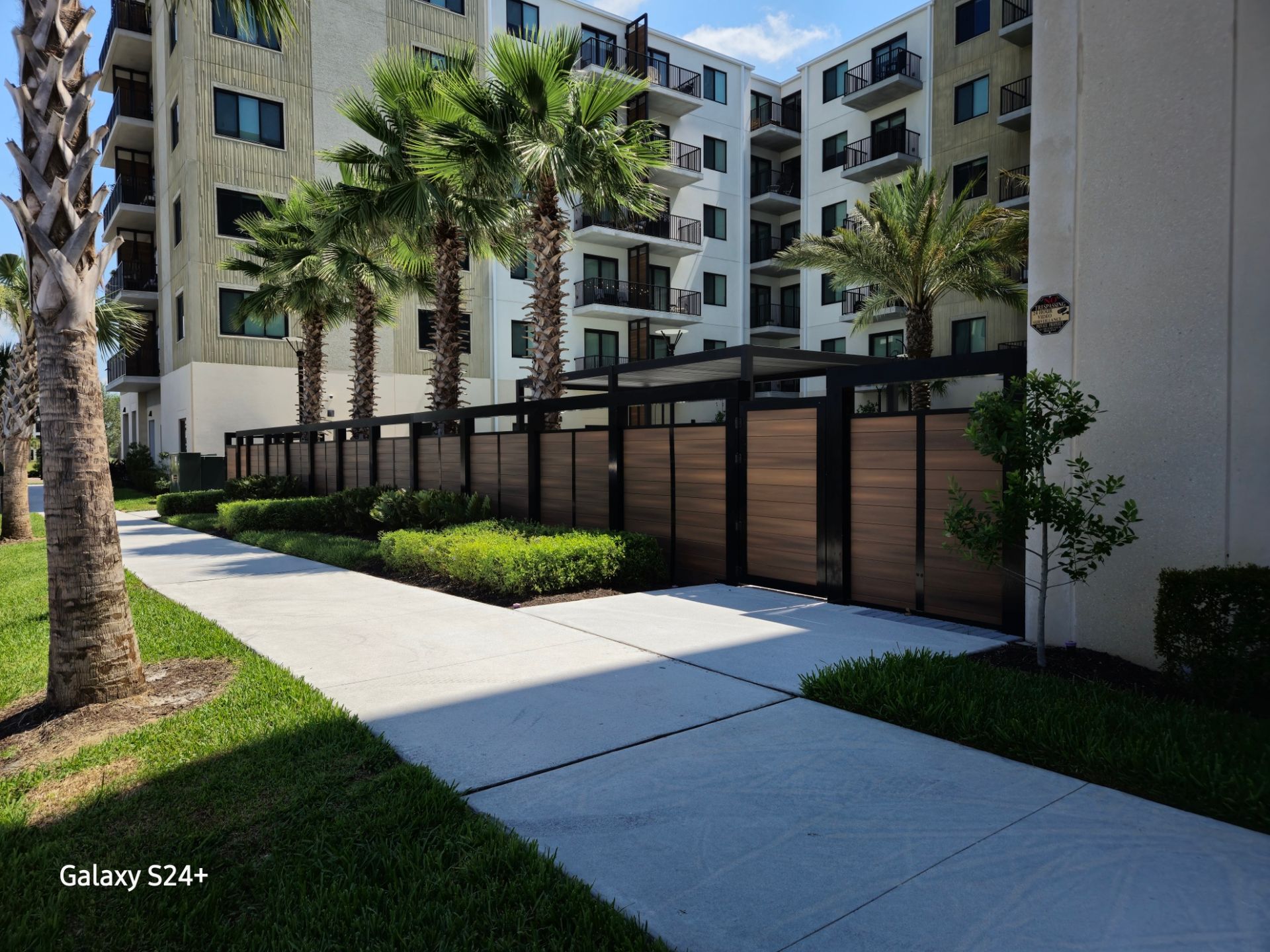 A building with a fence and palm trees in front of it.