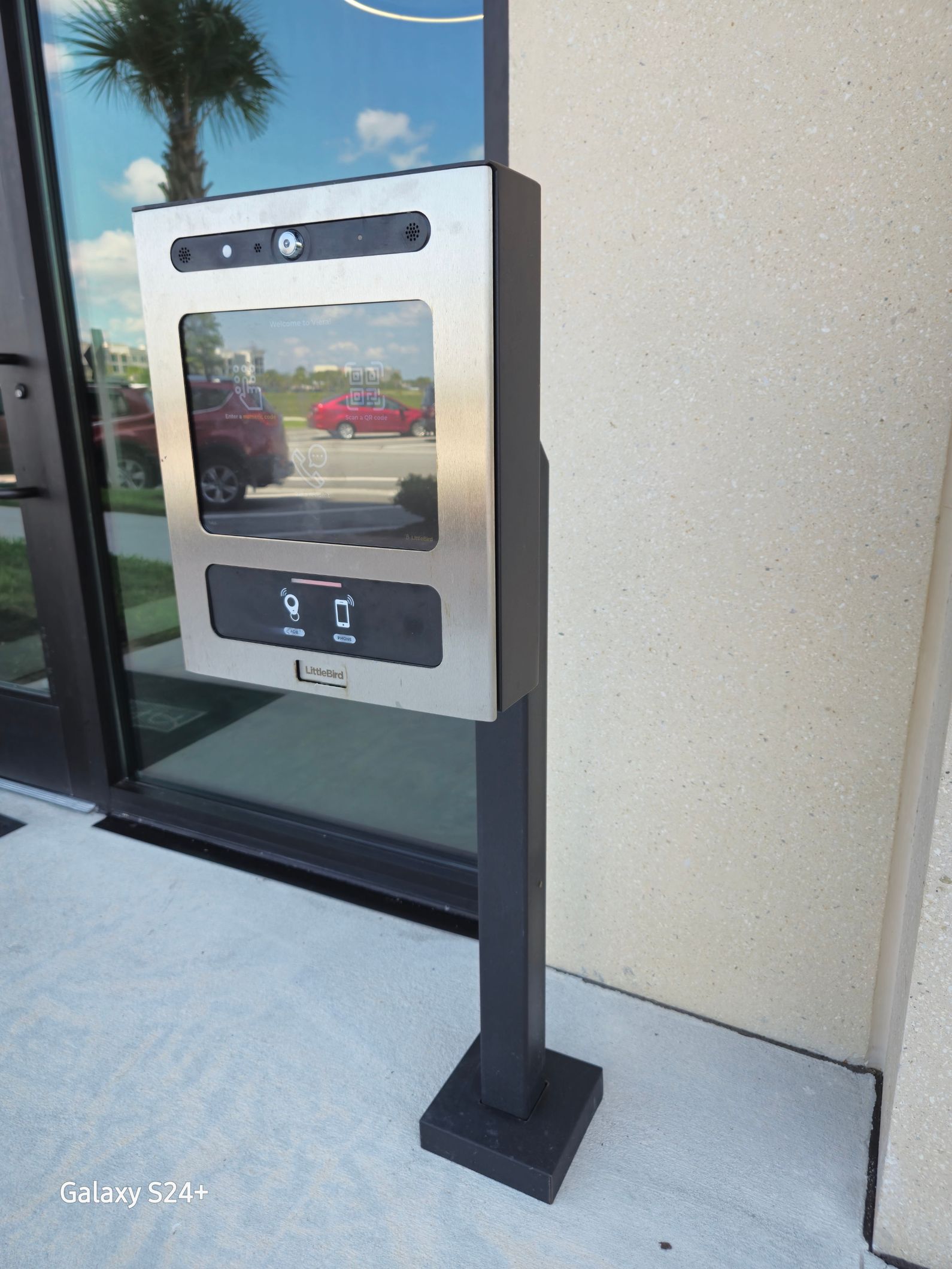 A stainless steel box on a pole outside of a building.