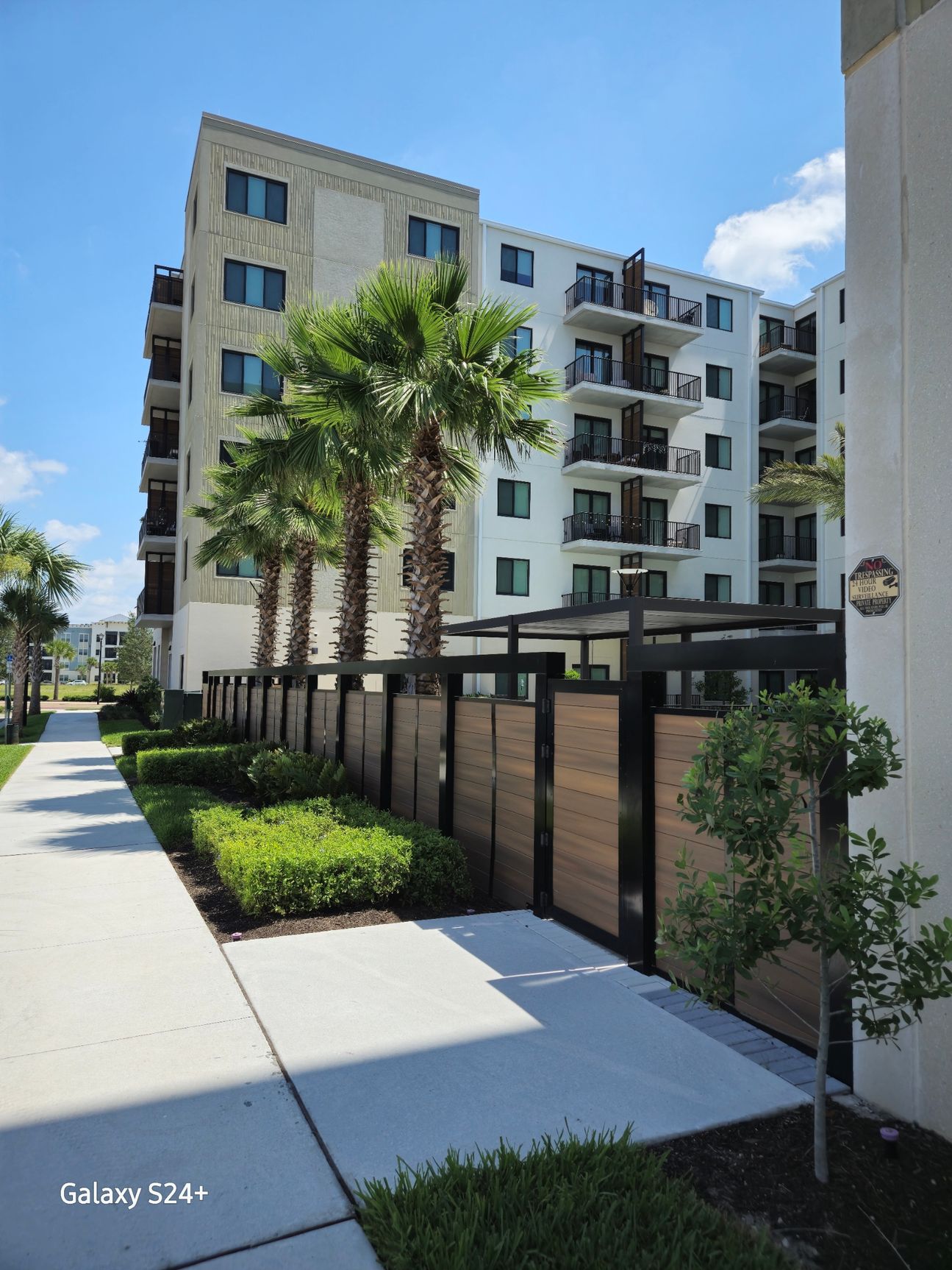 A building with a fence and palm trees in front of it.