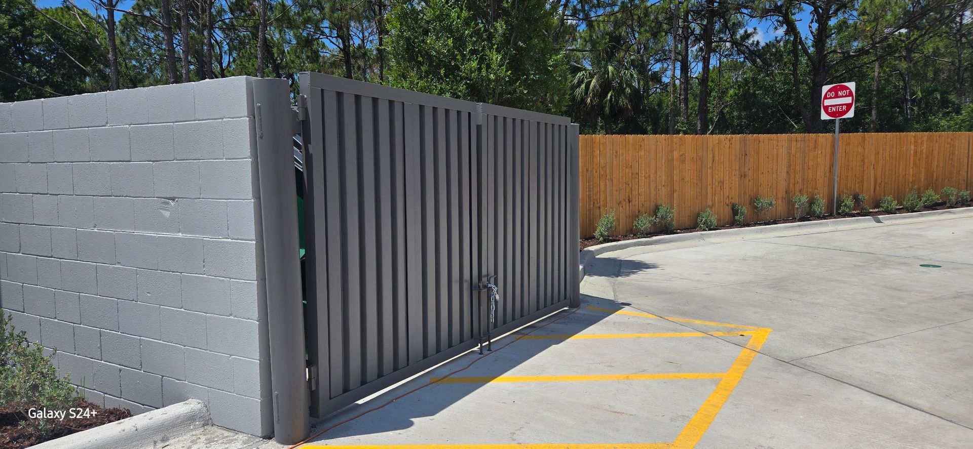 A sliding gate is sitting in a parking lot next to a wooden fence.