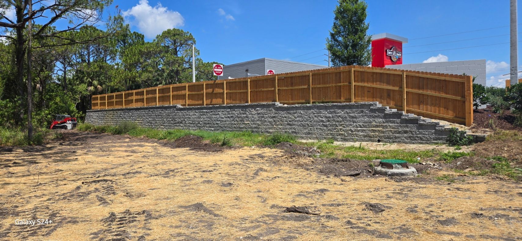 A wooden fence is surrounding a dirt field in front of a building.