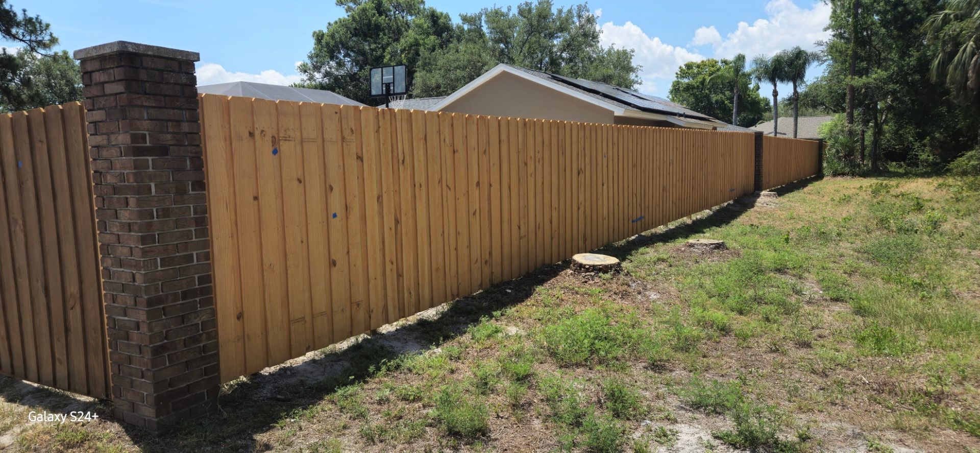 A wooden fence with a brick post in the middle of a grassy field.