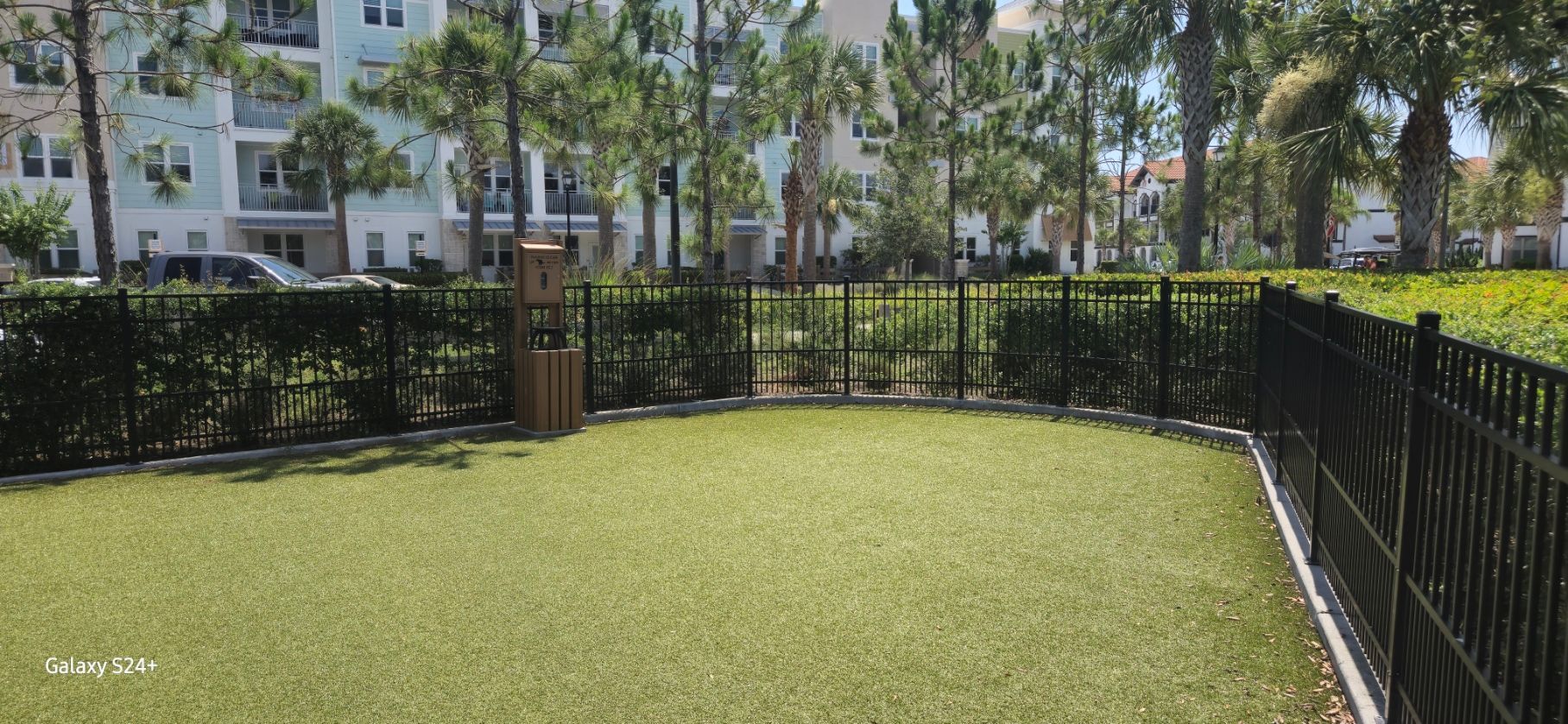 A black fence surrounds a grassy area in a park.