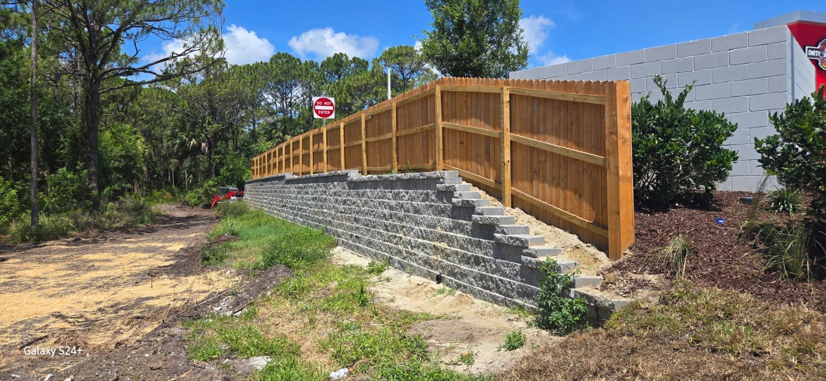 A wooden fence is sitting on top of a stone wall next to a road.