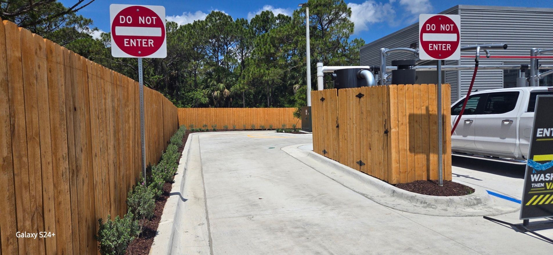 A do not enter sign is on the side of a road next to a wooden fence.