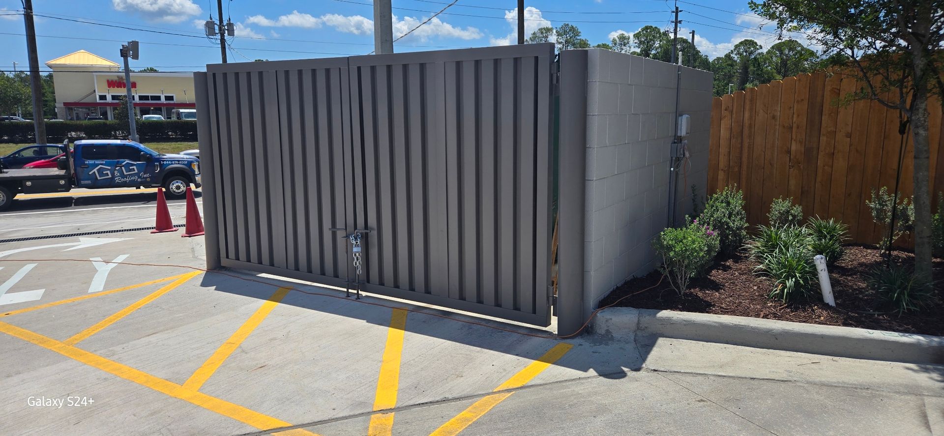 A sliding gate is sitting in a parking lot next to a building.