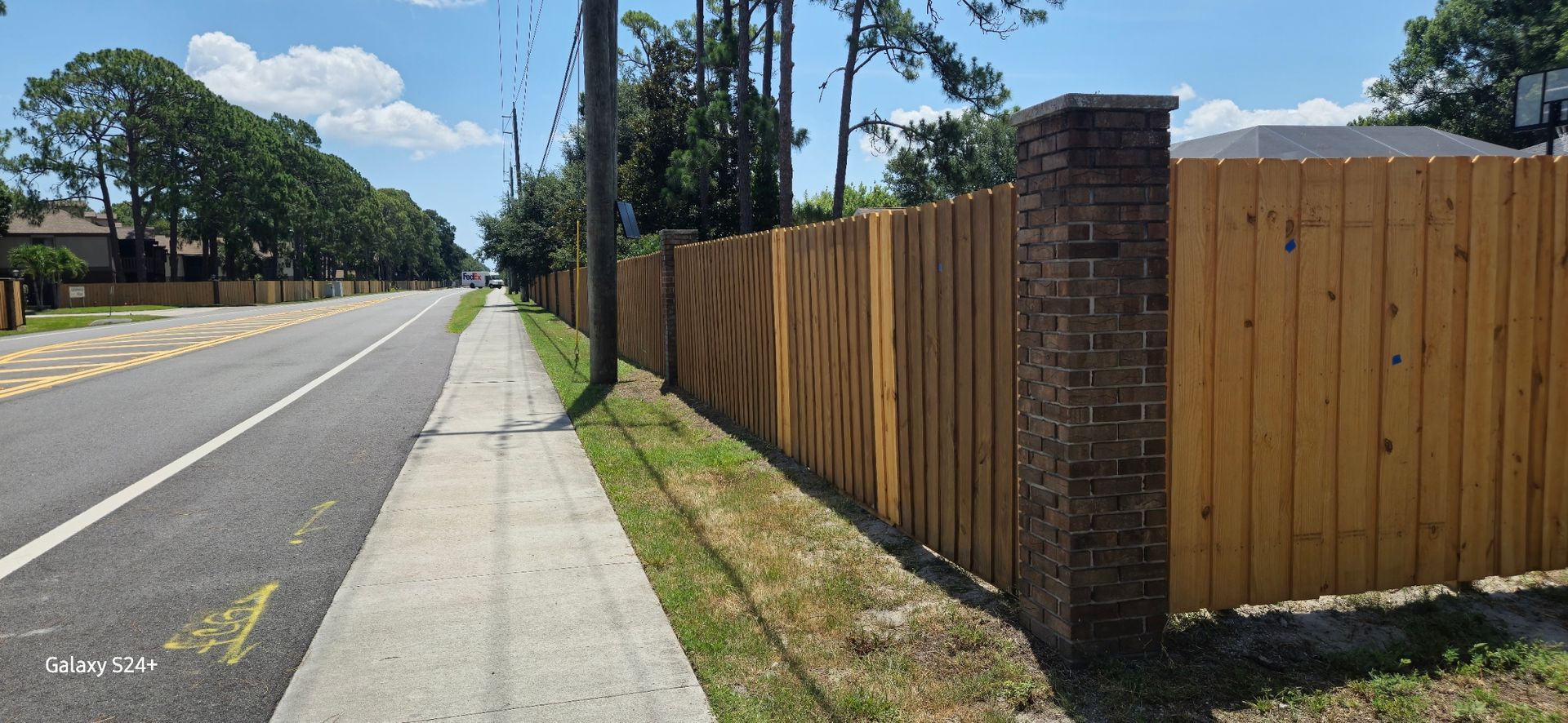 A wooden fence along the side of a road next to a sidewalk.