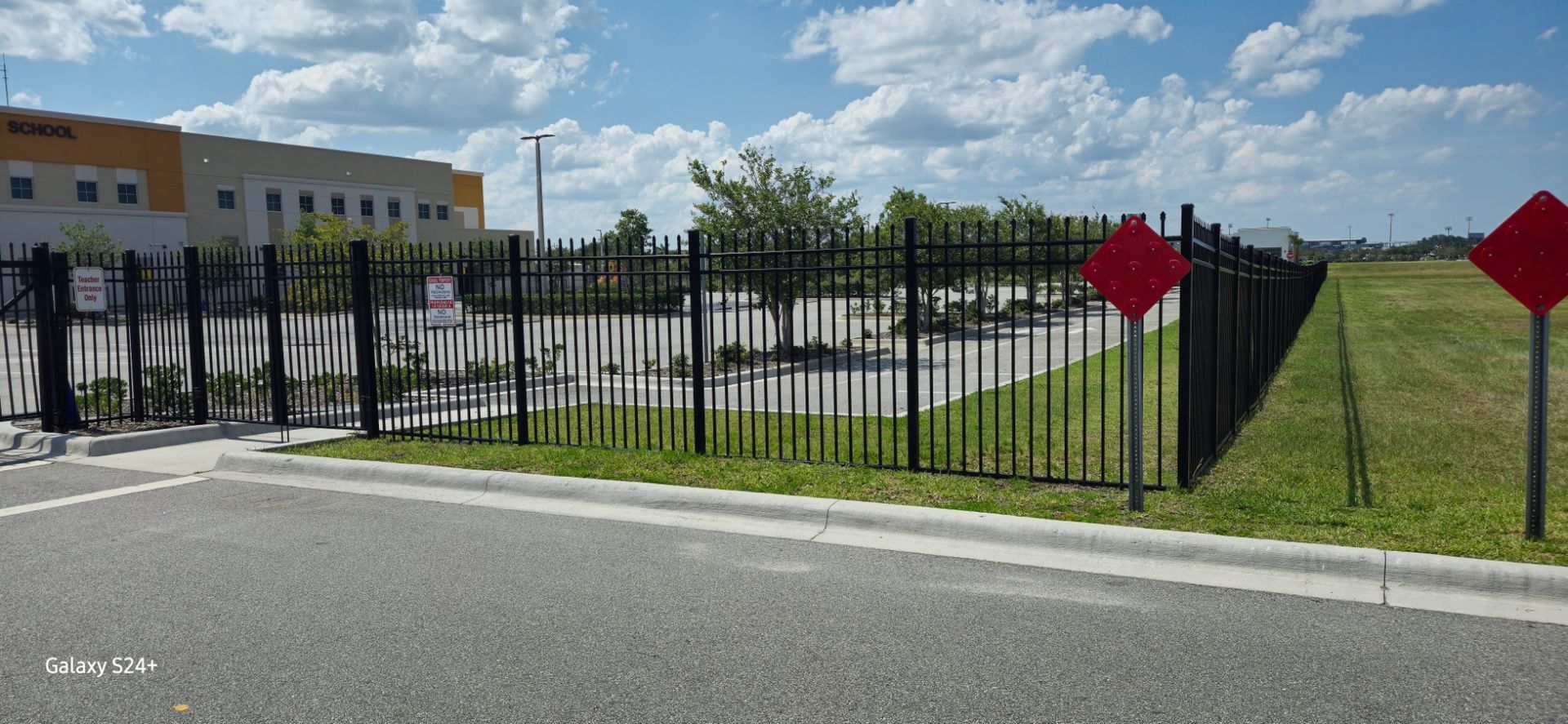 A red sign on the side of the road next to a fence.