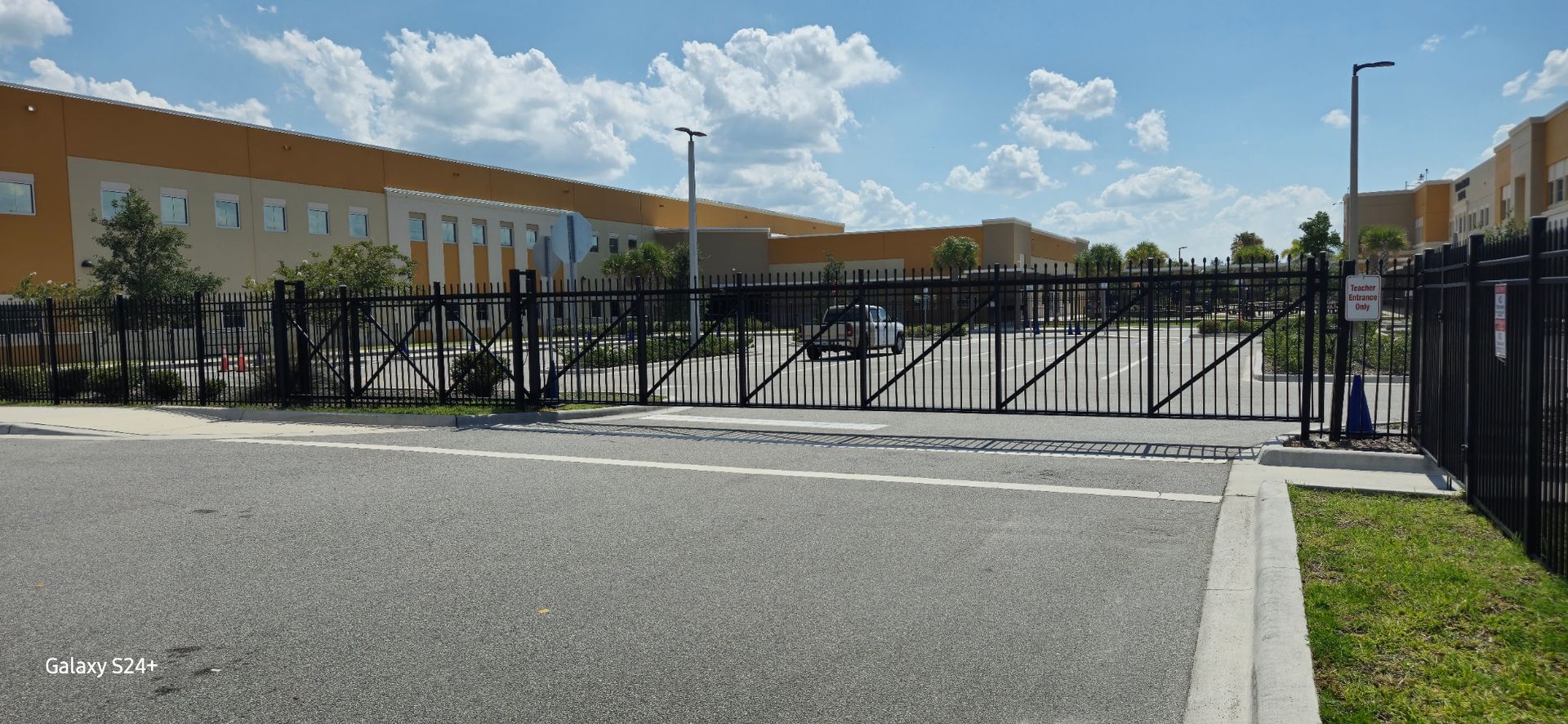 A fence surrounds a parking lot in front of a large building.