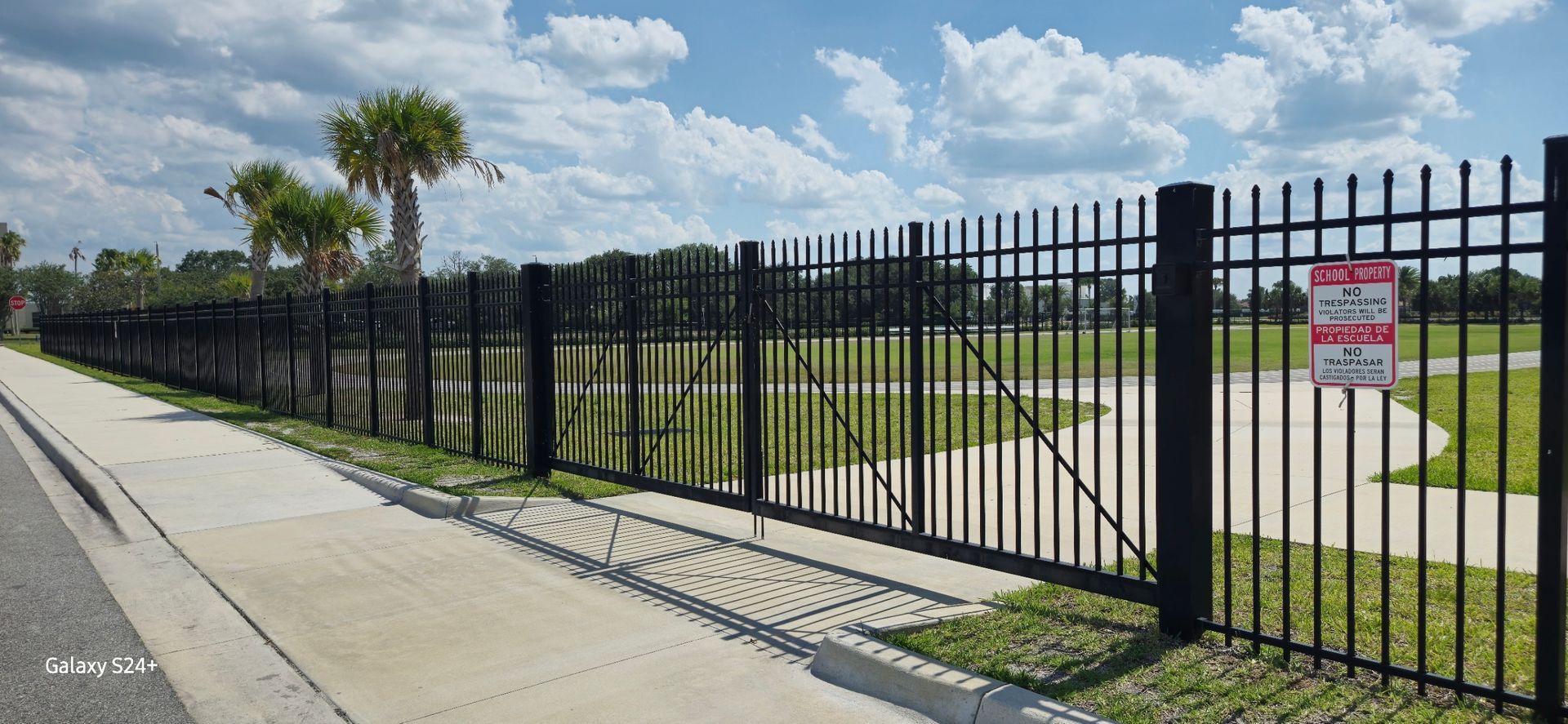 A black metal fence surrounds a park with a sign that says no parking.