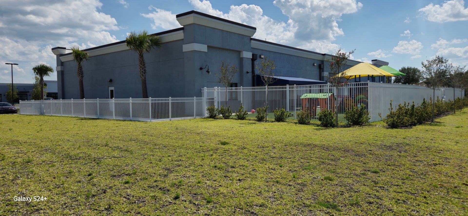 A large building with a white fence and a yellow umbrella in front of it.