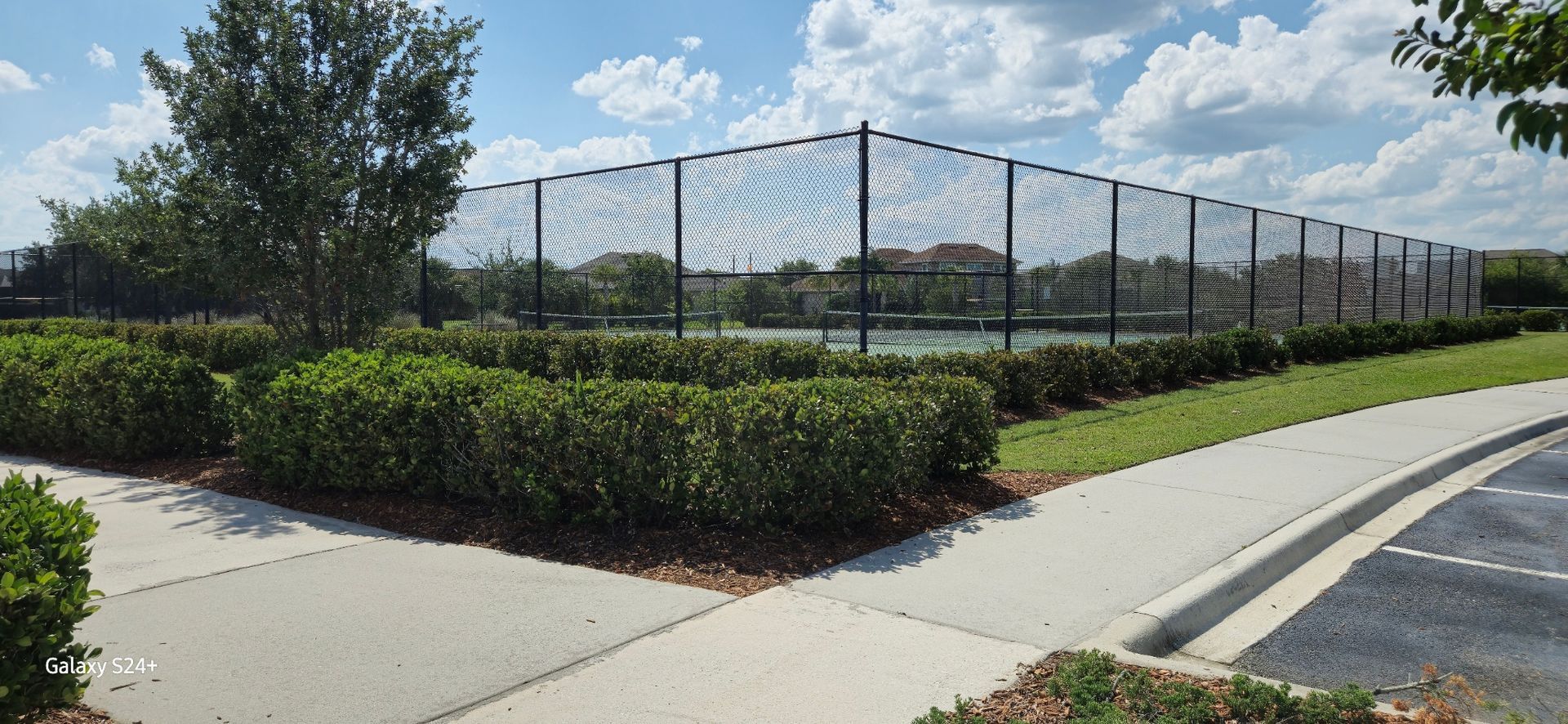 A tennis court is surrounded by a fence and a sidewalk.