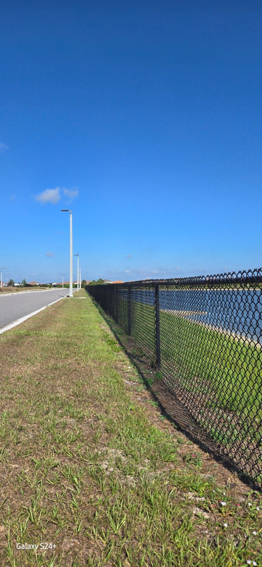 A chain link fence along the side of a road next to a body of water.