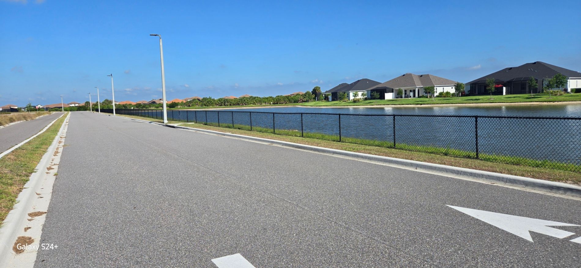 A road with a white arrow pointing to the right and a lake in the background.