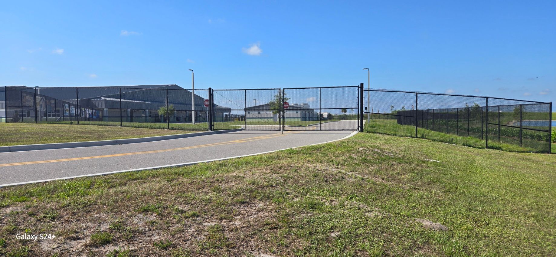 A fence surrounds a grassy field next to a road.