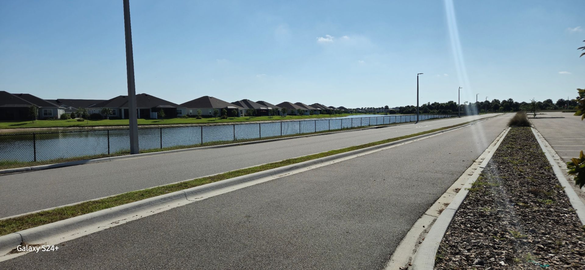 A road with a lake in the background and houses on the side.