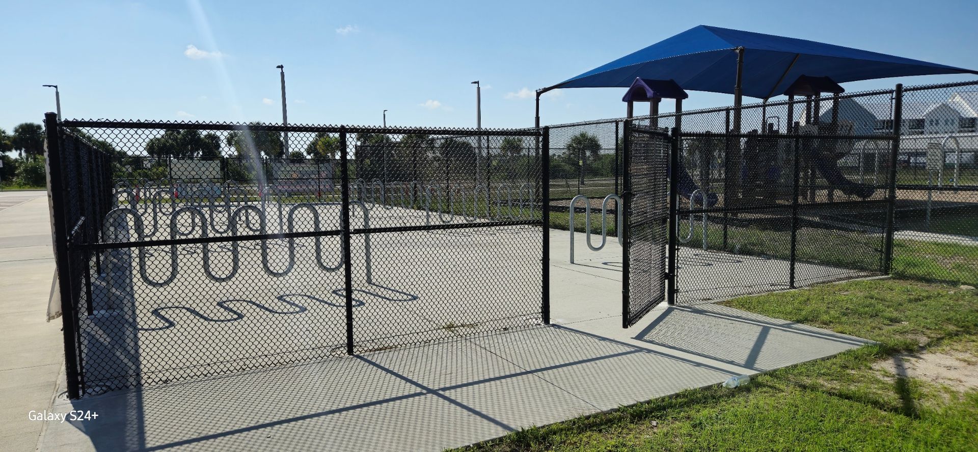 A chain link fence surrounds a playground with a blue umbrella.