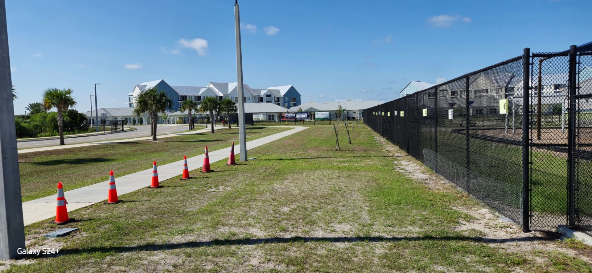 A chain link fence surrounds a grassy area next to a sidewalk.