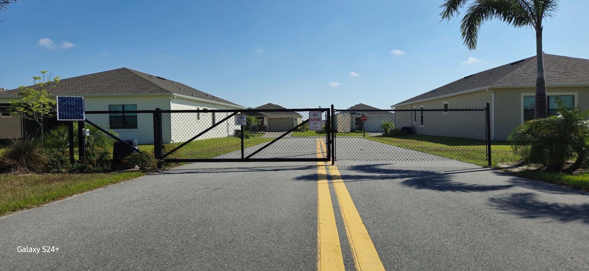 A gated entrance to a residential area with houses on the side of the road.
