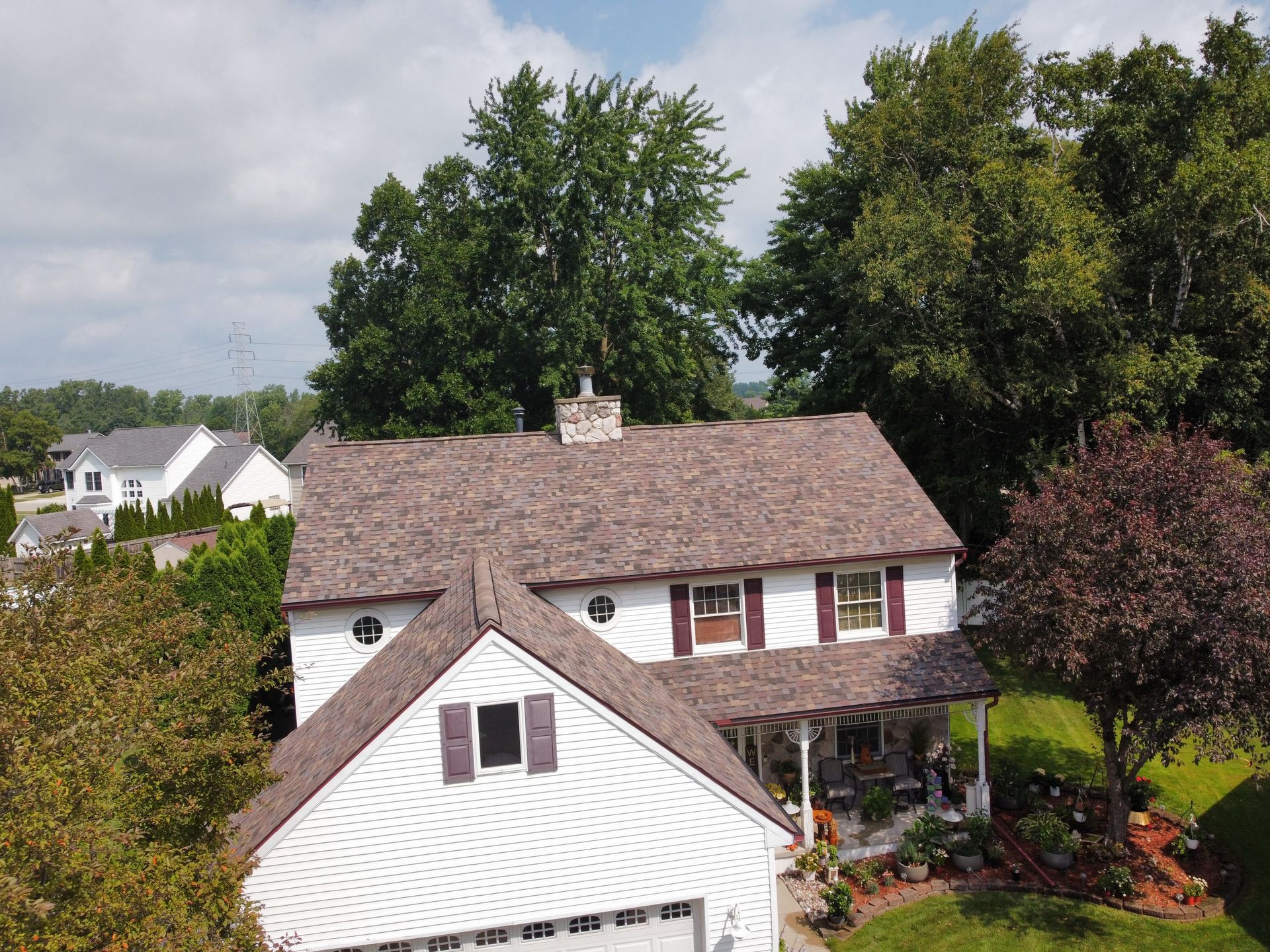 Suburban house with white siding, brown roof, and landscaped front yard under cloudy sky