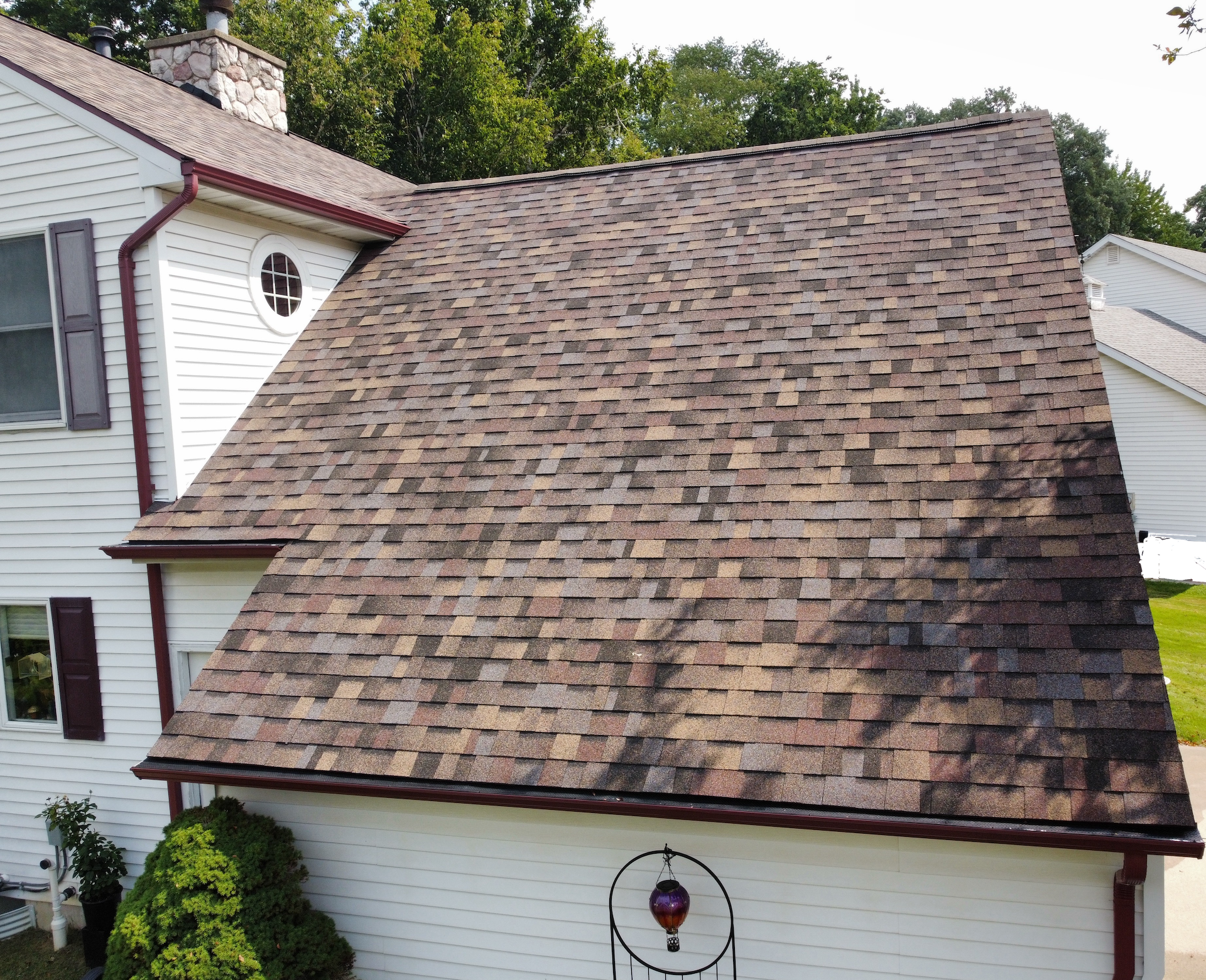 House with steep shingled roof and white siding, viewed from the side in a suburban setting