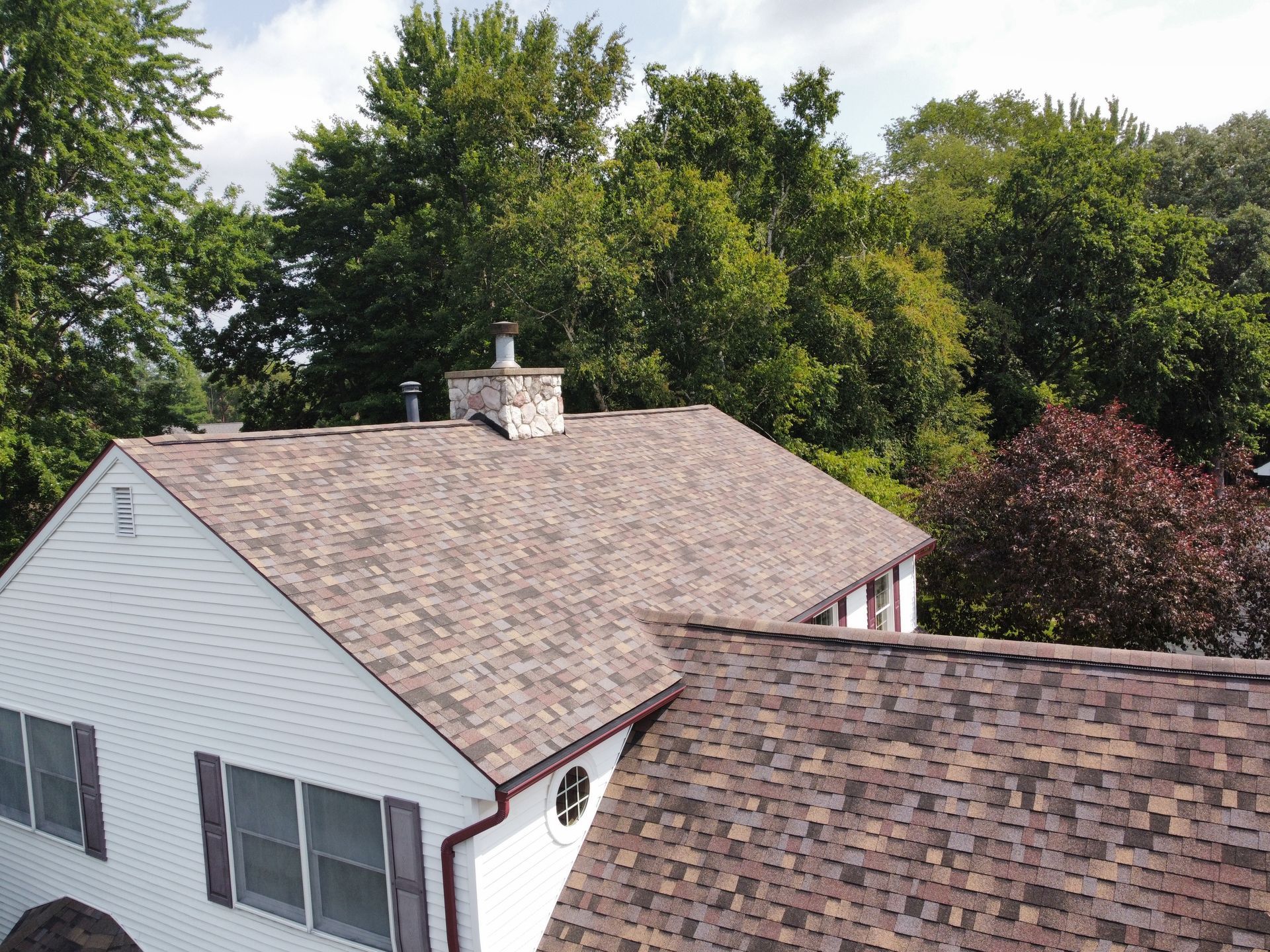 Aerial view of a white house with a shingled roof surrounded by trees.